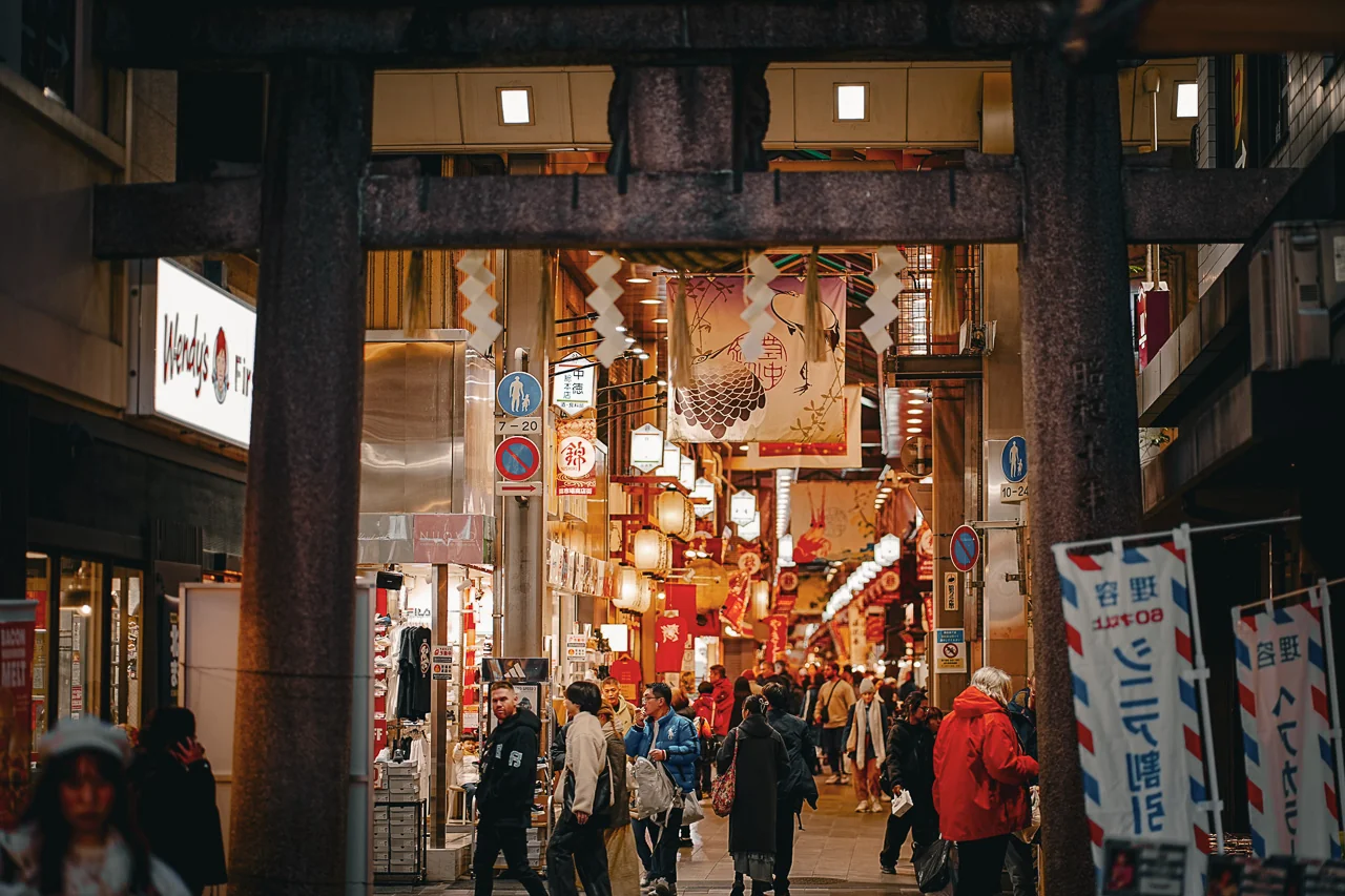 京都錦市場夜景，傳統木造店舖間掛滿紅色祭典燈籠，熙攘遊客穿梭於古老商街