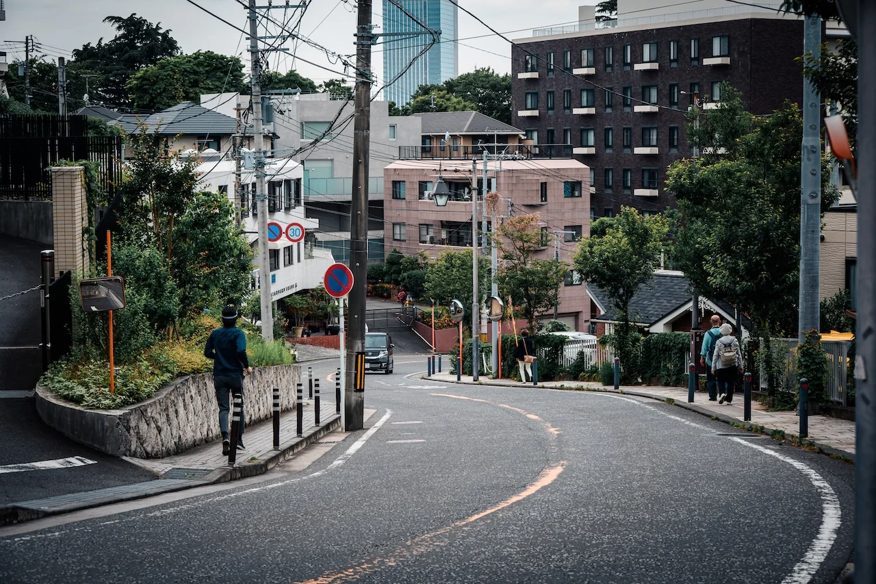 橫濱山手區街道彎角，行人與古老建築映襯於綠樹之間