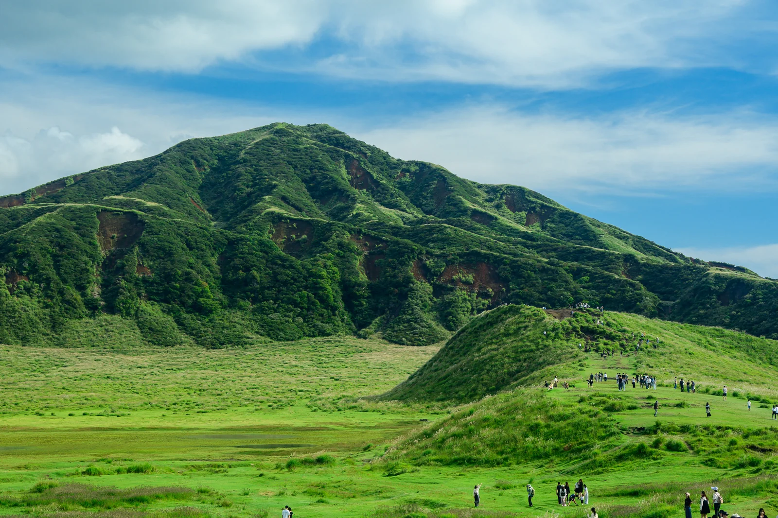 草千里綠色草原與米塚火山錐，遊客散佈